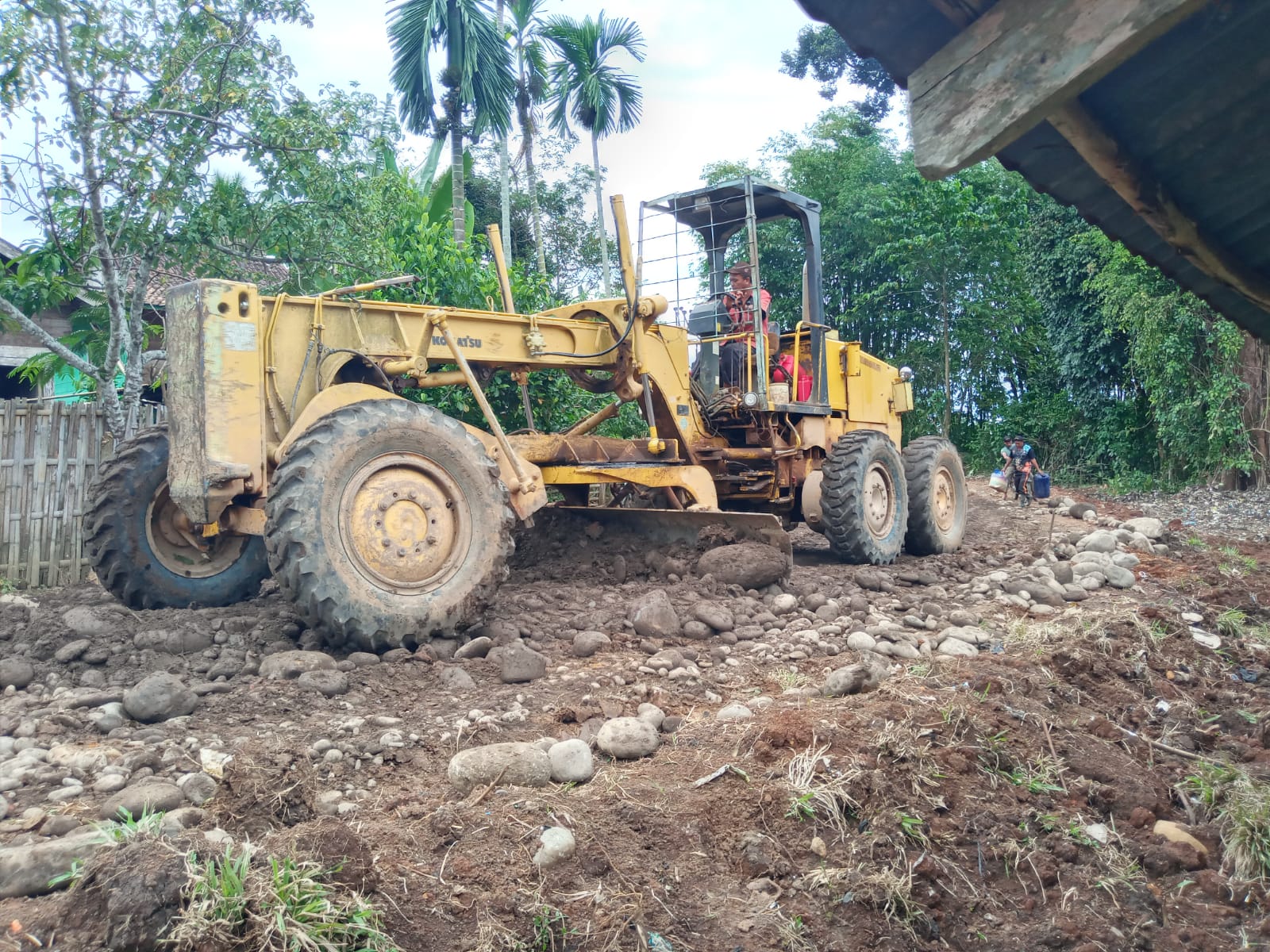 Alat Berat Grader Lakukan Skrap Material Bebatuan untuk Pengerasan Akses Jalan